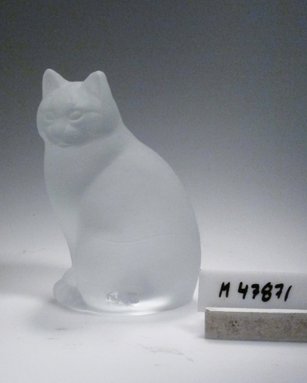 "Kattskulptur".
Beskrivning: Sittande katt.
Färg: Ofärgat klarglas, mattat.
Teknik: Stöpt och syrad.
Märkning: Genomsynlig etikett med silvertext. Se "Signering, märkning" ovan.
Inskrivet i huvudkatalogen 1996?
Funktion: Prydnadskatt