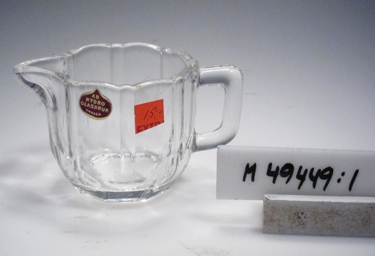 Sockerskål.
Färg: Ofärgat klarglas.
Teknik: Pressad, slätvärmd, planslipad.
Mått: Ovan anges största diameter. Fotdiameter: 52 mm.
Märkning: Etikett med lila botten, guldram och text. Se "Signering, märkning" ovan.
Inskrivet i huvudkatalogen 2007.'

Se även tillhörande gräddkanna M 49449:2.
Funktion: Sockerskål