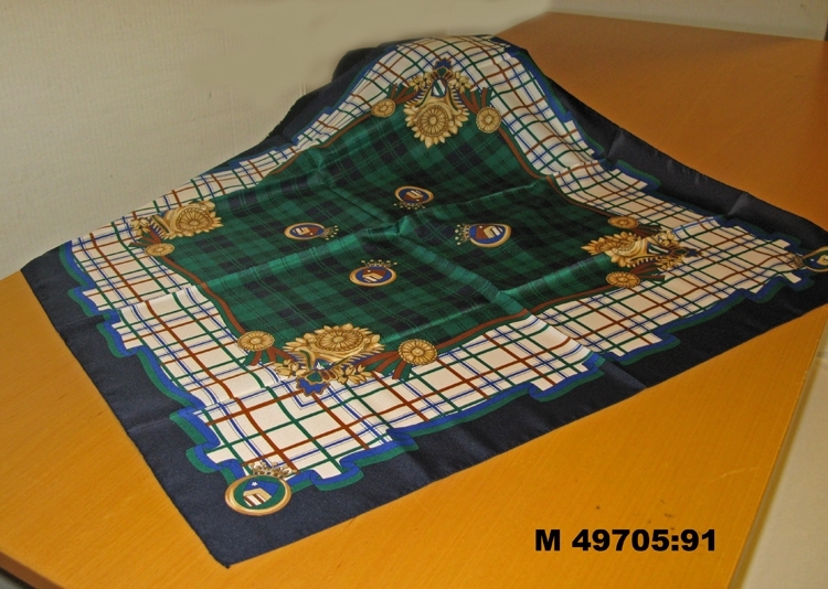 Scarf med blå kant. Bård med vit botten och bruna,gröna och blå smala ränder i rutmönster. 
Mitten med blått och grönt rutmönster. Tryck med vapensköldar.
Troligen aldrig använd; ligger i originalförpackningen


Inskriven i huvudbok 2010-01-04


















.





Inskrivet i huvudbok 2009-12-30