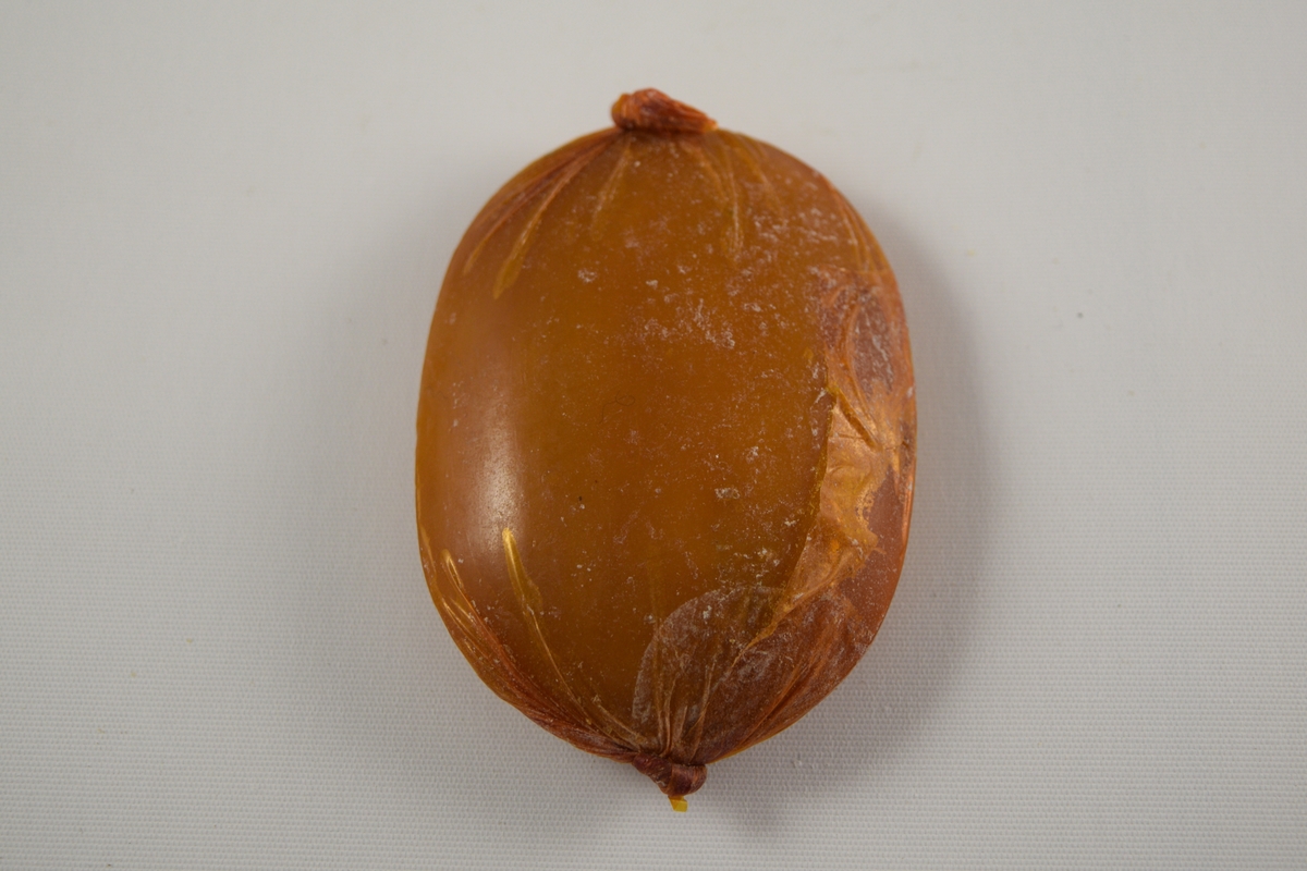 Oval såpe, seks stykker som er tilnærmet like. Produsert ved Saanums Sepefabrikk i Mandal. Tre stykker pakket i oransje plastikk (a-c), en i brun plastikk (d). To uten plastemballasje (e-f), men i ulik farge. Alle dekorert med Mandals kommunevåpen, med tre laks.