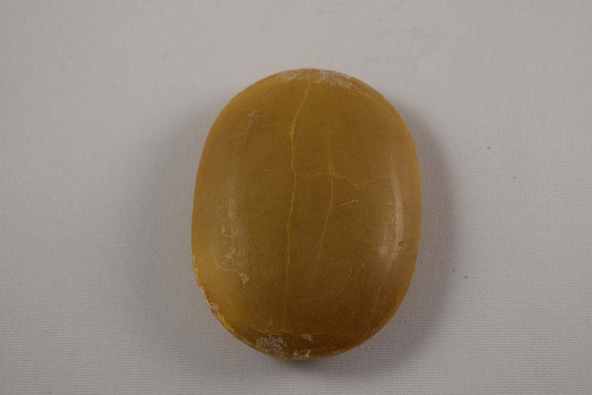 Oval såpe, seks stykker som er tilnærmet like. Produsert ved Saanums Sepefabrikk i Mandal. Tre stykker pakket i oransje plastikk (a-c), en i brun plastikk (d). To uten plastemballasje (e-f), men i ulik farge. Alle dekorert med Mandals kommunevåpen, med tre laks.