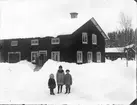 Barnen på gårdsplanen är Astrid, Valborg och Holger, barn till Stina och Lars Jonsson. Männen på bron till Gammelgården är okända. Gården ligger i Östansjö.