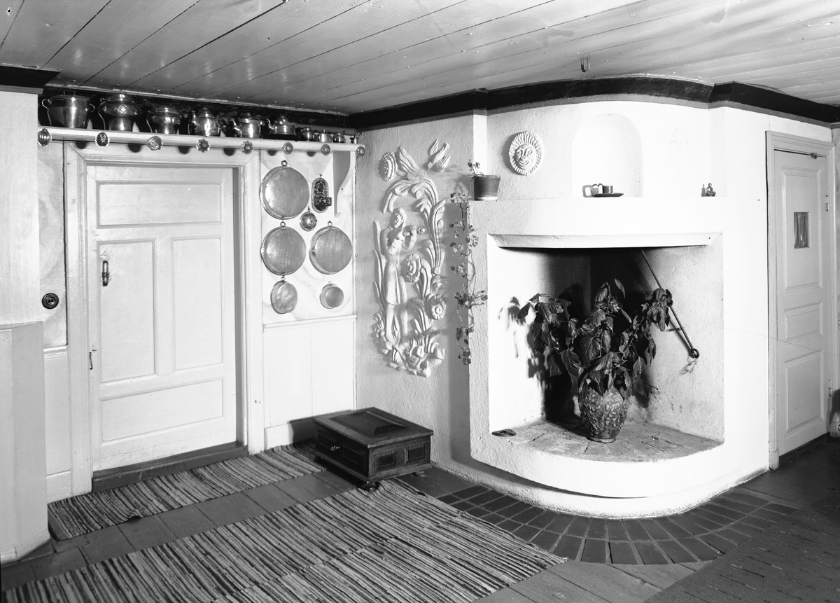 Från boken "Svenska Hem i ord och bilder" från 1944. Hemma hos Konstnären Manne Östlund, ägaren till Jons i Västbyggeby. Den öppna spisen med stuckrelief av Manne Östlund. På golvet skrinet för gårdsarkivet.
