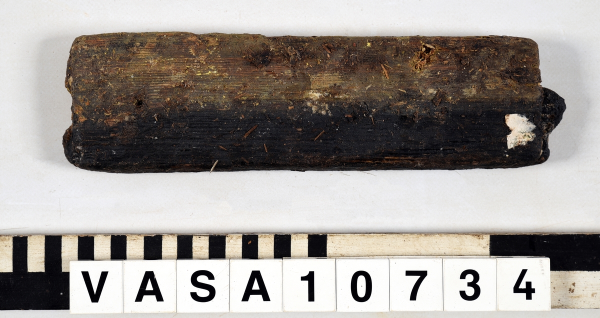 Odekorerad rektangulär bräda med ett spikhål. Tapp på båda ändarna möjlig spont på långsidan. Mycket vittrad yta. Kraftig saltskada (Salt 4) Tapparna avsplittrade.