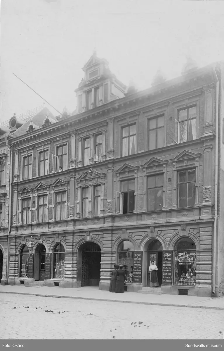 Karin Jonssons hus på Storg. 27 innan det revs. Fröken Jonsson står här i dörren till Mesch & Jonssons missionsbokhandel samt leksaksaffär. Missionsbokhandeln drev hon tillsammans med sin kompanjon Eva Mesch (gift Liljeblad) som avled 1922. Karin Jonsson avled 1948 och dessförinnan hade affären övertagits av Elin Hydén.