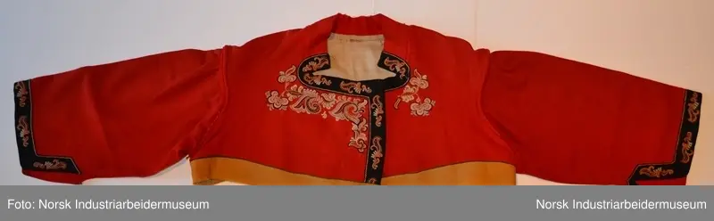 Rød tøye til Anne Bamle-bunad. Gul kanting sydd fast nederst på trøya. Kanten langs åpningsfolden og deler av halsen er svart og brodert med plattsøm. Svart kant med plattsøm-broderi. Bak på trøya er det en illudert klokke(folder) i ryggen og klipte taggekanter. Halsen på trøya er buet, noe som var vanlig på de tidlige bunadene Anne Bamle lagde. Trøya er ellers brodert med plattsøm på forsiden. 

Trøya (ikke ermene) er foret med et tynt, beige silke-/bomullstoff. Trøya har trekvartlange ermer.