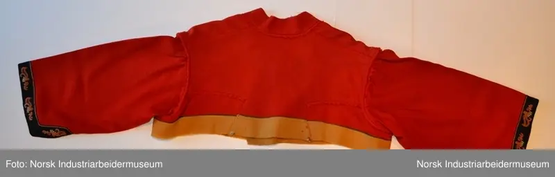 Rød tøye til Anne Bamle-bunad. Gul kanting sydd fast nederst på trøya. Kanten langs åpningsfolden og deler av halsen er svart og brodert med plattsøm. Svart kant med plattsøm-broderi. Bak på trøya er det en illudert klokke(folder) i ryggen og klipte taggekanter. Halsen på trøya er buet, noe som var vanlig på de tidlige bunadene Anne Bamle lagde. Trøya er ellers brodert med plattsøm på forsiden. 

Trøya (ikke ermene) er foret med et tynt, beige silke-/bomullstoff. Trøya har trekvartlange ermer.