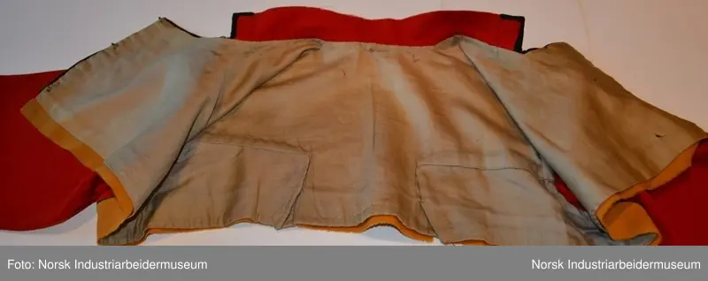 Rød tøye til Anne Bamle-bunad. Gul kanting sydd fast nederst på trøya. Kanten langs åpningsfolden og deler av halsen er svart og brodert med plattsøm. Svart kant med plattsøm-broderi. Bak på trøya er det en illudert klokke(folder) i ryggen og klipte taggekanter. Halsen på trøya er buet, noe som var vanlig på de tidlige bunadene Anne Bamle lagde. Trøya er ellers brodert med plattsøm på forsiden. 

Trøya (ikke ermene) er foret med et tynt, beige silke-/bomullstoff. Trøya har trekvartlange ermer.