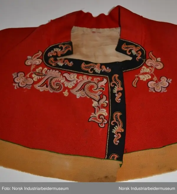 Rød tøye til Anne Bamle-bunad. Gul kanting sydd fast nederst på trøya. Kanten langs åpningsfolden og deler av halsen er svart og brodert med plattsøm. Svart kant med plattsøm-broderi. Bak på trøya er det en illudert klokke(folder) i ryggen og klipte taggekanter. Halsen på trøya er buet, noe som var vanlig på de tidlige bunadene Anne Bamle lagde. Trøya er ellers brodert med plattsøm på forsiden. 

Trøya (ikke ermene) er foret med et tynt, beige silke-/bomullstoff. Trøya har trekvartlange ermer.