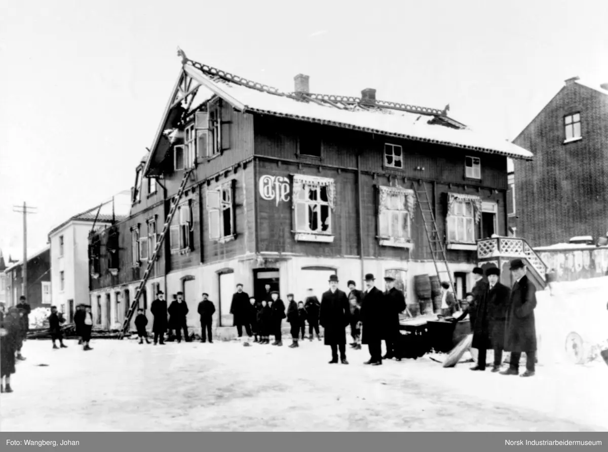 Brann i Telegata kafe (Cafe). Taket er betydelig skadet, mennesker stående rundt, stige opptil vindu i annen etasje.