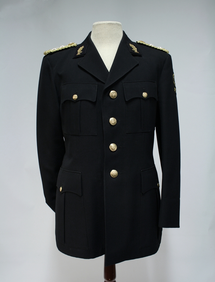 Uniform for politinspektør etter 1963-reglement med merking etter 1977-reglement. Helårsuniform M/1963 med skjorte, langbukse, belte, helårskappe og jakke. Skyggelue med gullbrodert bånd, loslue og båtlue M/1967. Kappen og jakken har skulderklaffer av flettede gullsnorer med to sølvstjerner og festeknapp i gullbroderi. Skjorten har en enklere skulderklaff med to gule render og to sølvstjerner. Det følger med et ekstra enkelt lærbelte og et ekstra sett skulderklaffer til skjorte. Plaggene har gullfargede løveknapper.