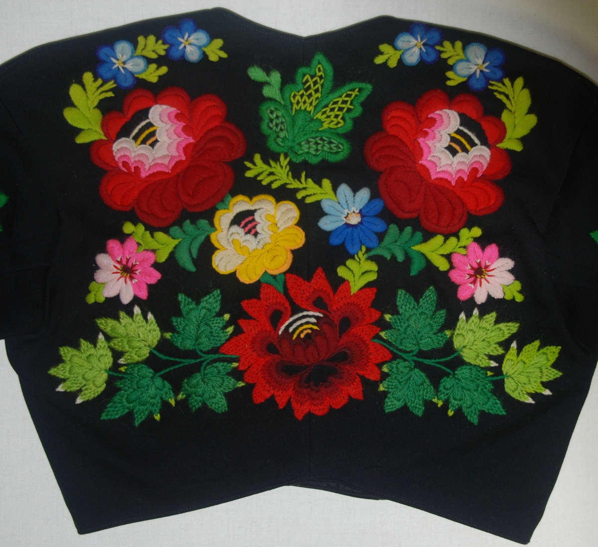 Tröja från Floda, Dalarna. På svart kläde broderi i ullgarn i livligaste färger: blommotiv i en viss stilisering. Fodrad med svart satin.
Äldre katalogisering av Elisabeth Thorman (enl. uppgift).