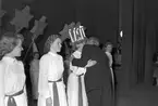 Mary Forslund, Gävle Lucia 1949. Hon är 21 år och handhar arkivet hos A/B Carl Larssons fotografiska atelier Tärnorna är Margareta Svensson, Harriet Jansson, Ulla Persson och Marianne Lundin. Luciatåget startar från Brandstation och går Nygatan - N. Skeppargatan - Drottninggatan - Stora Esplanadgatan och åter till Brandstationen. Soaré på teatern som arrangerat av köpmanna- och hantverkarungdomen i Gävle, leds av Macce Kjellin, kröntes Lucian med smycket av direktör Gösta Nygren, Furuvik. Lucia tävlingen arrangerades av Norrlands-Posten.