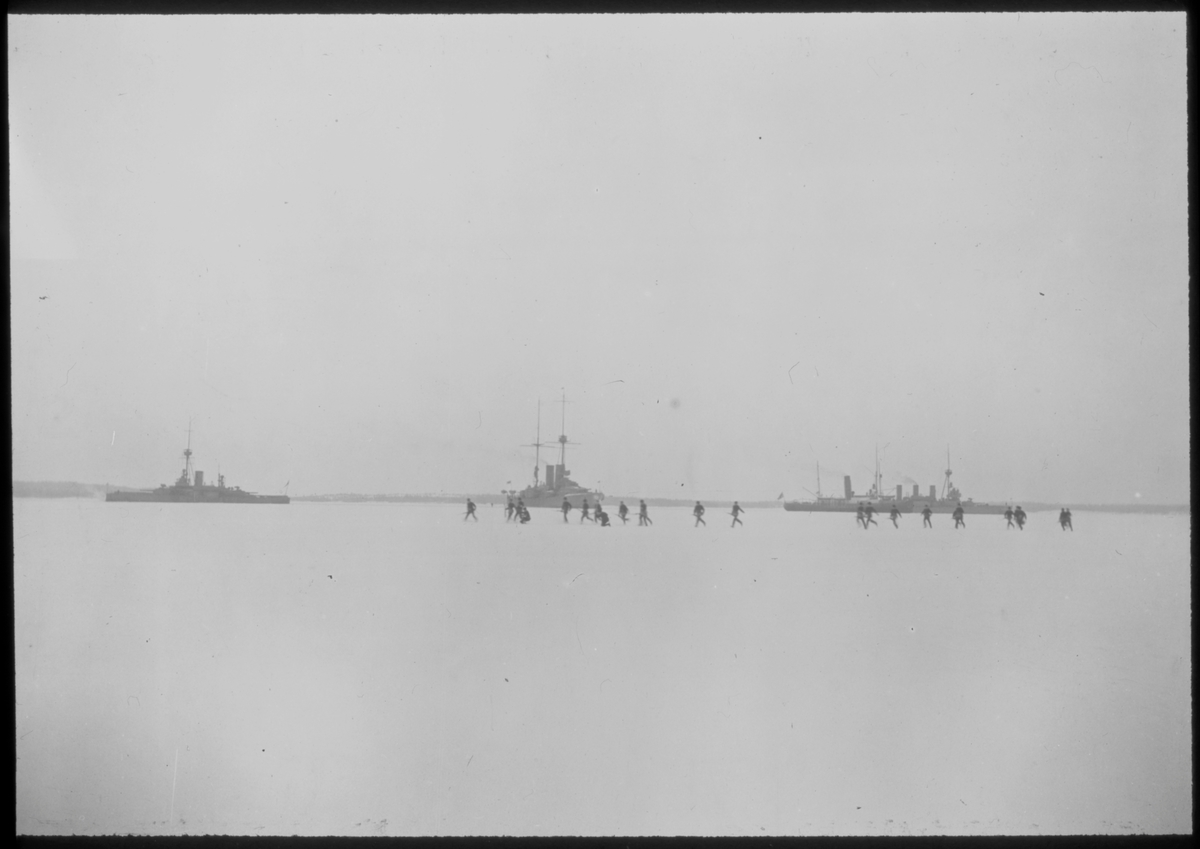 Svensk militär under språngmarsch på isen framför fartyg i den svenska eskadern under Ålandsexpeditionen 1918. I bakgrunden ses från v till h pansarskeppen THOR och SVERIGE, isbrytaren ISBRYTAREN II samt pansarskeppet OSCAR II.