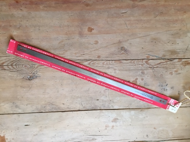 Ubrukt sagblad montert på originalt forpakning bestående av en rektangulær papp-plate. I enden av papp-platen er festet en hyssingstump for opphenging på vegg. Trolig er bladet beregnet til en grindsag.