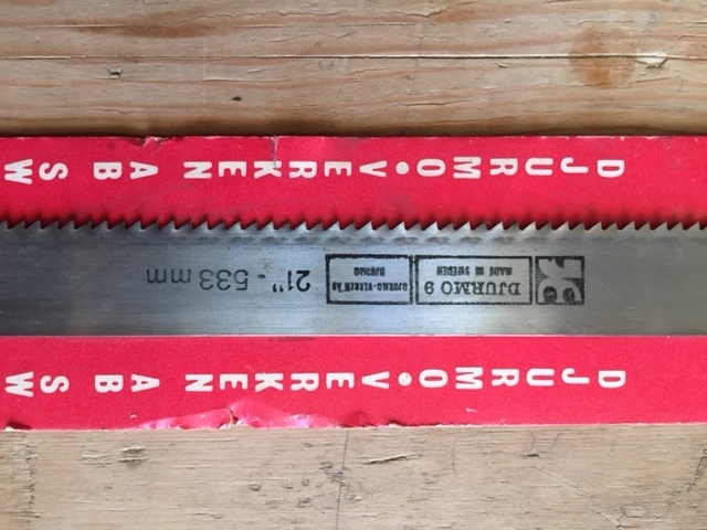 Ubrukt sagblad montert på originalt forpakning bestående av en rektangulær papp-plate. I enden av papp-platen er festet en hyssingstump for opphenging på vegg. Trolig er bladet beregnet til en grindsag.