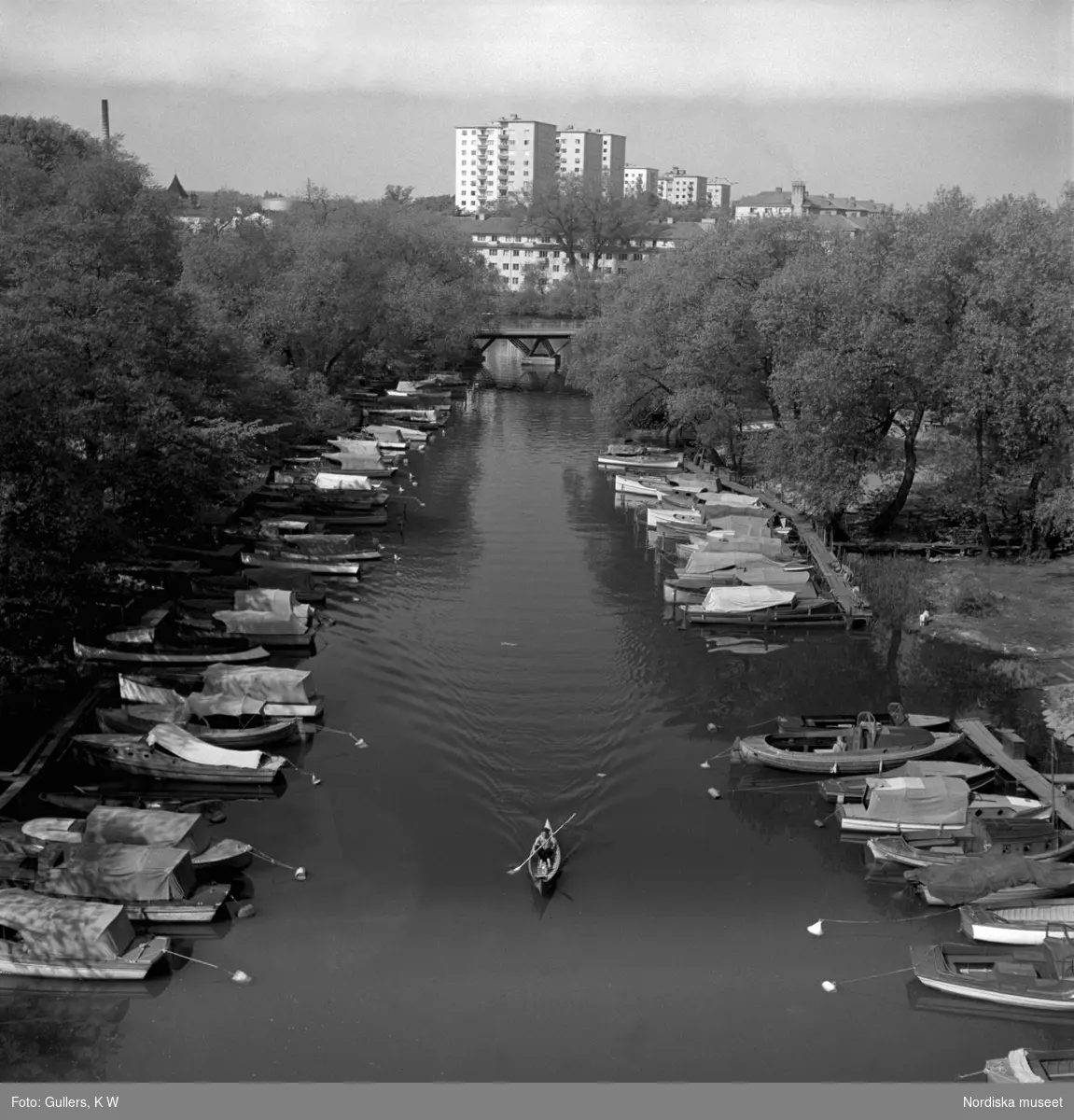 Pålsundet, Stockholm. En ensam kanotist mellan förtöjda fritidsbåtar. Bebyggelse på Reimersholme i bakgrunden.