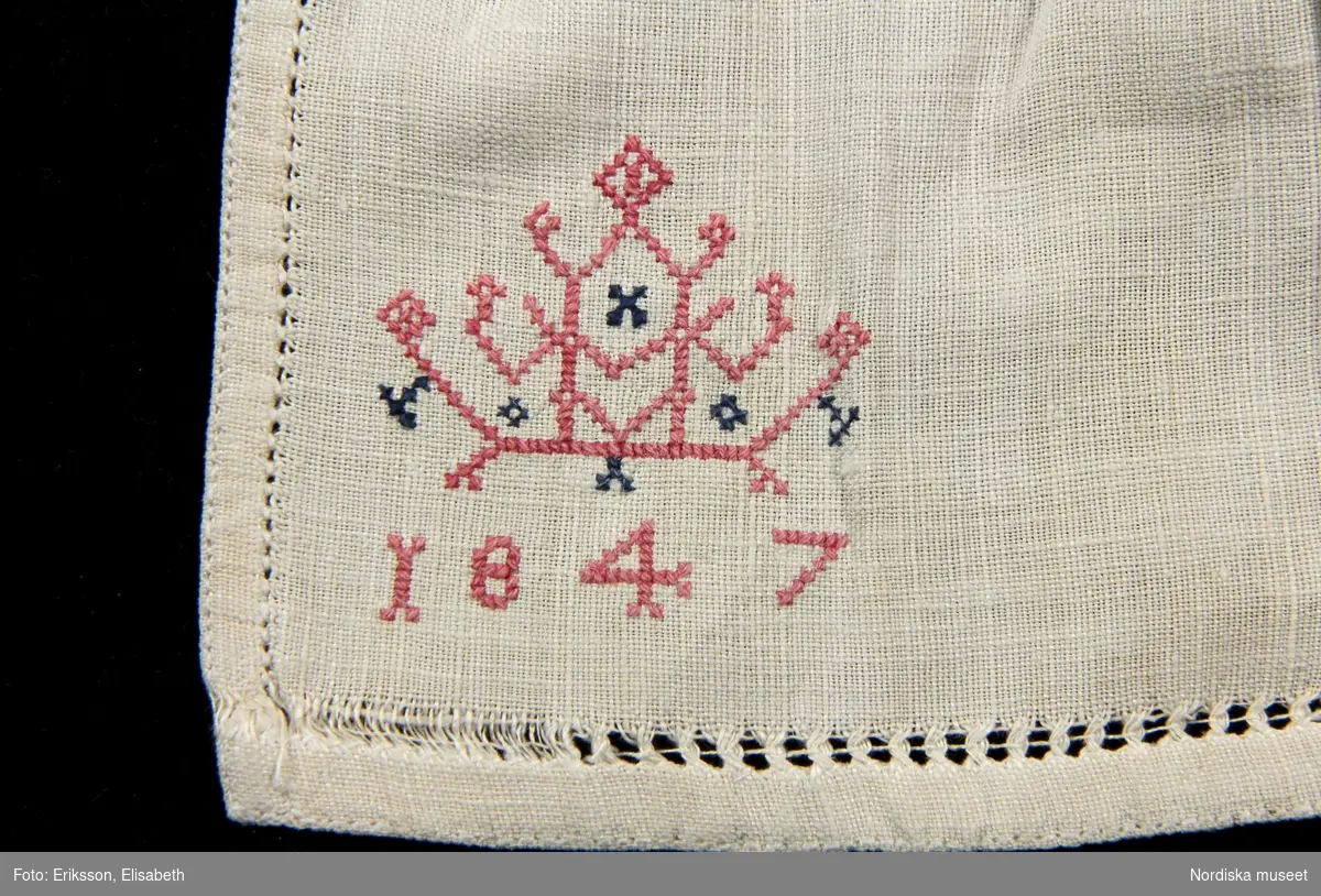 a. Kvinnokrage i form av ett rynkat krås, av halvlinnelärft med rosa korssömsbroderi, märkt MAD 1847
b. Tillhörande länkknapp av mässing.
/Berit Eldvik 2010-09-21