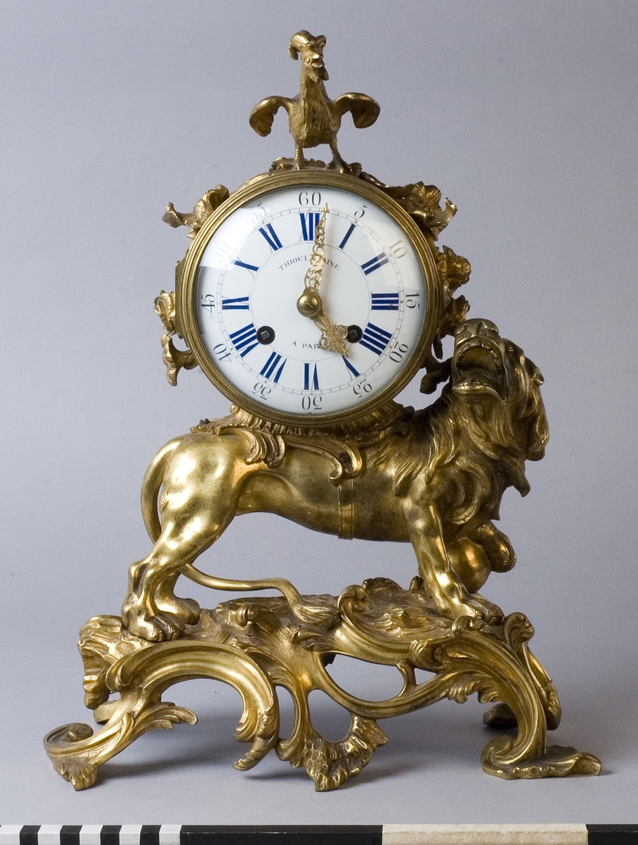 Urhuset i form av en tunna som står på ett rytande lejon med ena foten på ett klot på ett genombrutet rocailleornament. Ovanpå tunnan står en galande tupp, på sidorna rosor och växter.