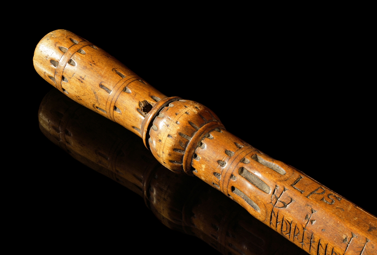 Kalenderstav i form av åttkantig, stavformad runkalender. 
Det korta handtaget har en balusterformigt utförande, med vertikala spetsar runt tvärgående band. Initialer: L P S och inskriptionen 1634 under handtaget och svagt på stavens ände.

S:t Peders lek (med korrektur). En gammal utslagningslek som går ut på att skilja vänner från fiender. Med hjälp av stavens markeringar kunde lekledaren i hemlighet räkna ut vilka personer som skulle slås ut. Namnet syftar på aposteln Petrus roll som himmelrikets portvakt, där han skiljer hedningar från kristna.