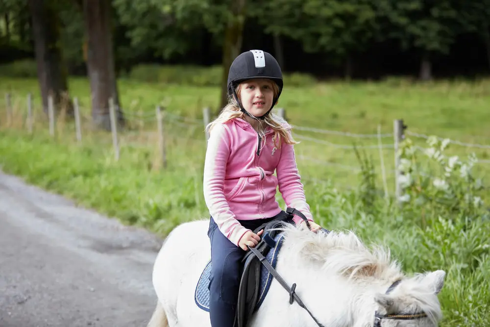 En jente rir på en hvit ponni. 