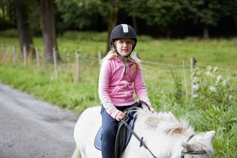 En jente rir på en hvit ponni. 