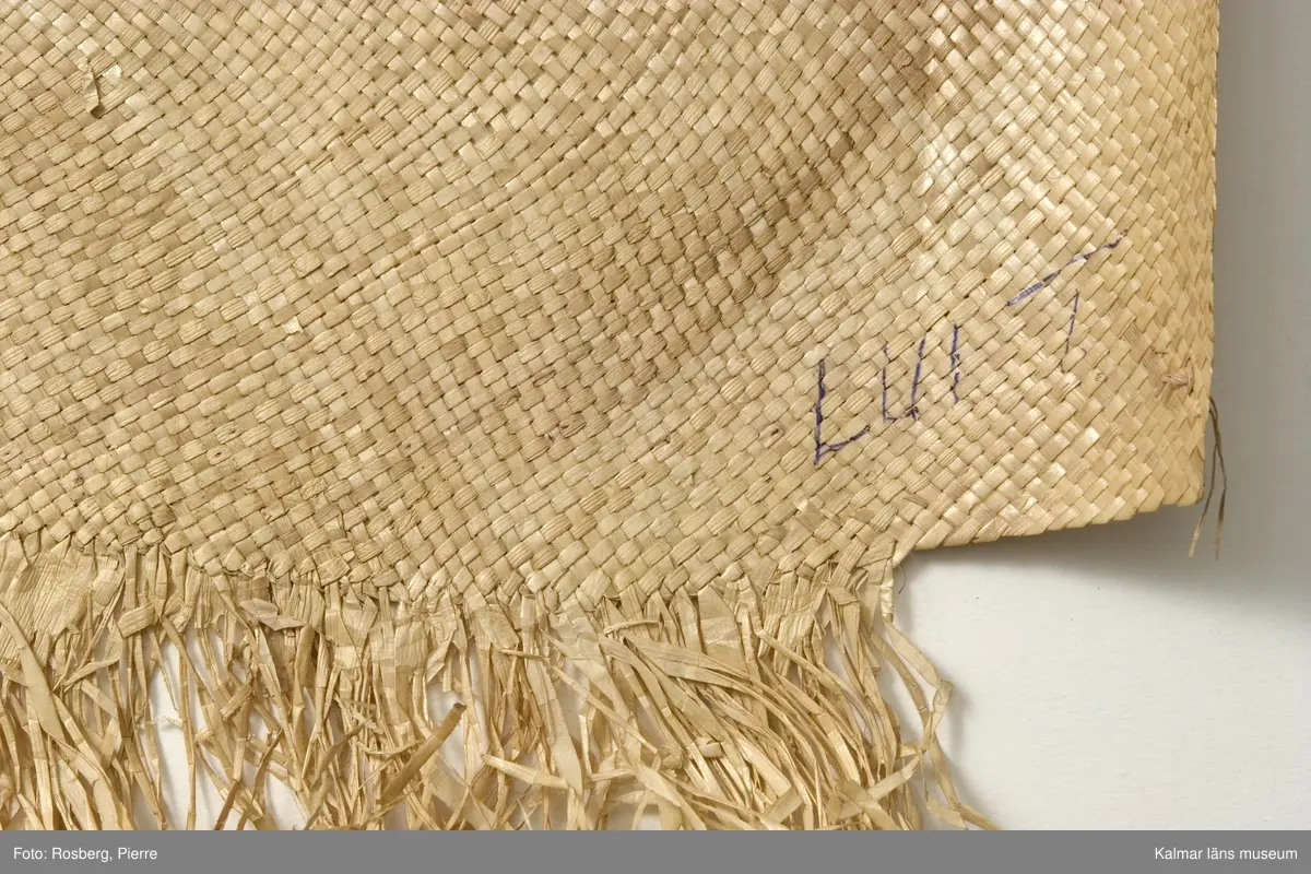 KLM 28465. Matta/kjol av pandanus (en palmväxt) och fjädrar. Plagget benämns 'ie toga. 'ie är en av tre sorters odlade palmväxter som används av samoanerna för mattorna. Mattan är mer att betrakta som ett ceremoniellt klädesplagg flätat av pandanus med fransar i båda ändarna och dekorerat med röda och några få vita fjädrar fastsydda med maskinsöm. Den här mattan, är ett ceremoniellt klädesplagg, den bärs runt midjan som en kjol, dubbelvikt så att man skall kunna se fransarna. Den hålls vanligen på plats av en gördel av barktyg. Följande namn finns påskrivna, på framsidan, KELEmet, TutuilA x Elsa, LUIT; på baksidan, AiLUA Poliko, LEALA SOLA. Därutöver ett nummer som tycks vara 10 finns också. Tutuila är för övrigt namnet på en sydöstsamoansk ö, vilken är huvudön i Amerikanska Samoa.