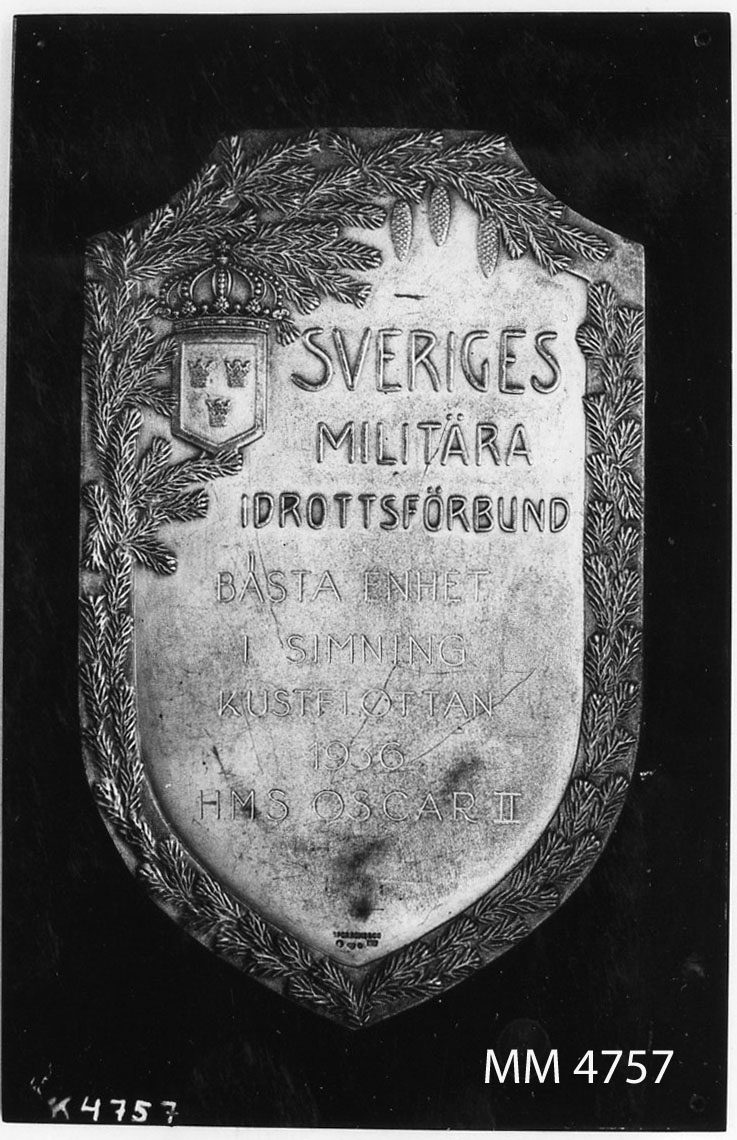 Plakett av silver, fast på svart ebonitplatta. Utgör pris i simning.
Text i relief: Sveriges Militära Idrottsförbund.
Ingravering: Bästa Enhet i simning Kustflottan 1936 HMS Oscar II.