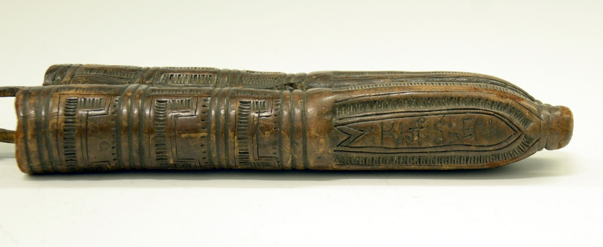 Fra protokollen: Tvislir med 1 kniv og belte av semska skinn med smøygjestolar av massing med ein nedhangande ring or kvar stol eller kvar sylgje. Beltekroken er bladforma, uthoggin (gravert) i strikmynster, fraa denne gjeng 7 taattar traadlekkje, av massing og forma som kyrmaal-taattar. Kniven med treskaft (barlind) og svære, støypte i massing - holkar (uthogne) støypte i rank eller strik. I enden paa bakholken kvardar rundt og krosslykkje i tverenden. Knivsbladet langt, med sneideslipa odd-fase i bakken. Slirine med fergd strik-ornamentik. Paa den eine innskrifti K.A.S.H, paa den andre: ANNO 1731.
Fra Telemarki eller Sæterdalen.