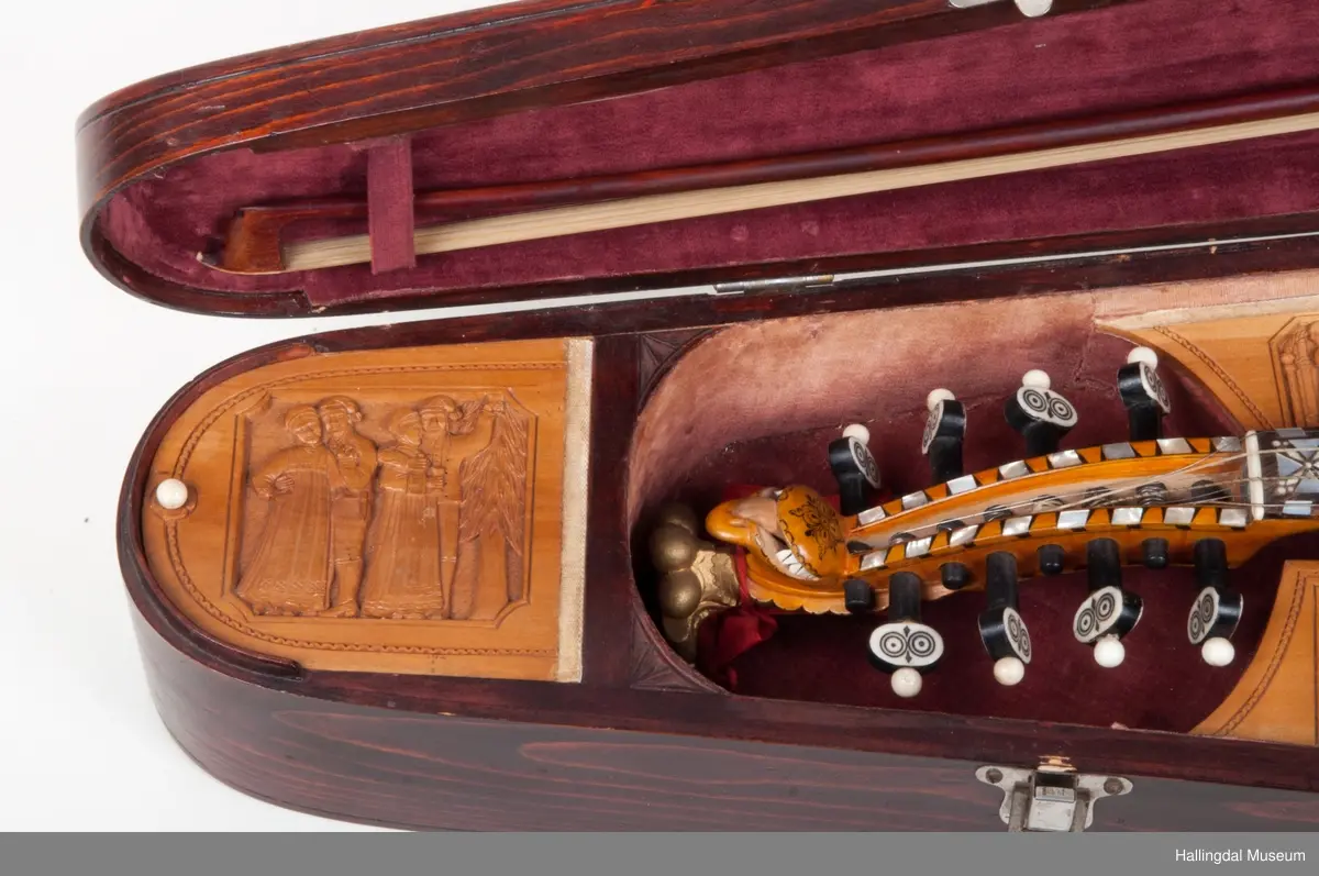 Lokket er utskjært med drake og båndslynginger.  Utskjæringer inne i felekassen.  5 rom med lokk i kassen.  3 lokk har utskjæringer med motiver fra hallingdans.  
Skaftet er besatt med perlemor, rosetegning i sort, dyrehode øverst på skaftet.  4 strenger over og 4 strenger under strengbrettet.  2 felebuer rødbrun mahogni.  Fela se HFN 03210.
