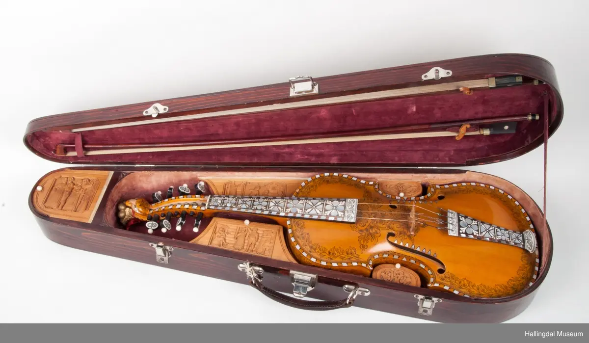 Lokket er utskjært med drake og båndslynginger.  Utskjæringer inne i felekassen.  5 rom med lokk i kassen.  3 lokk har utskjæringer med motiver fra hallingdans.  
Skaftet er besatt med perlemor, rosetegning i sort, dyrehode øverst på skaftet.  4 strenger over og 4 strenger under strengbrettet.  2 felebuer rødbrun mahogni.  Fela se HFN 03210.