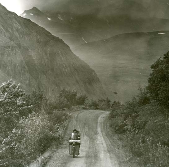 Norska fjäll ner mot Skibotn i Norge, augusti 1961. En Vespa med två personer kommer åkande på en grusväg mellan branta fjäll.