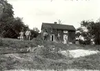 Ett slåtterlag framför en tvåvånings enkelstuga i Nästeshult 1914.