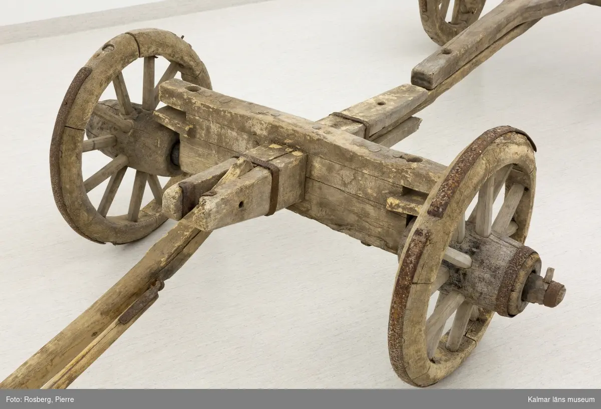 KLM 11833. Bultvagn, hästvagn. Av trä och järn. För hästar. Bultvagn som består av två hjulpar med två bankar, fyra träaxlahjul med järnbeslag, skakel samt dräkt. Det främre hjulparet är mindre än det bakre och har en tillhörande skakel som fästes i en träanordning på dess bank. Dräkten består av en kraftig rektangulär stång av trä med sex stycken borrade hål. Dräkten fästes i en annan träanordning som sitter på motsatt sida av skakeln på det främre hjulparets bank. På det bakre hjulparets bank sitter ett bågformat hål där dräkten sedan förs igenom för att sammankoppla vagnens delar samt justera dess längd. De bakre hjulens nav är dekorerade med zig-zag mönster.