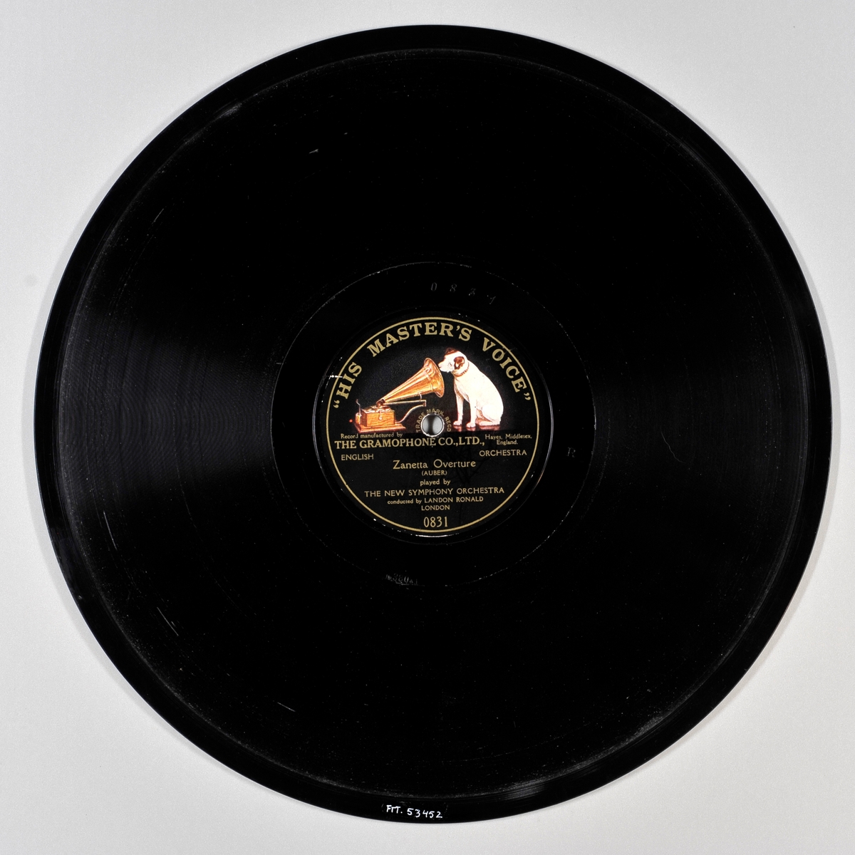 Svart plate med svart etikett med gullskrift. På etiketten er det bilde av en hund som sitter og lytter til en grammofon.