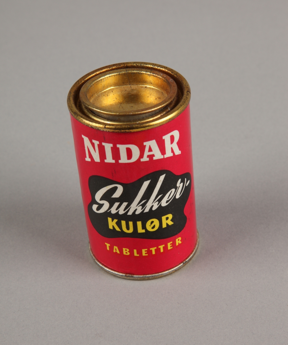 Liten sylinderformet boks med sukkerkulørtabletter. Rundt flatt lokk.