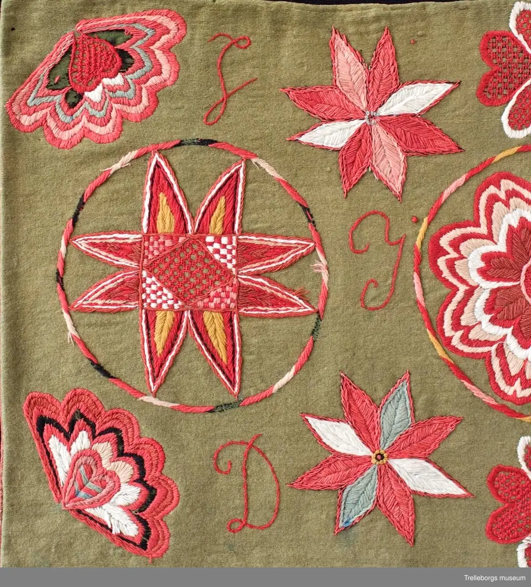 Bottentyg är grön vadmal. Tre stora ringar i kontur utgör huvudmotiv. I ringen i mitten är en stor blomma med 8 kronblad utfyllnad. I de båda ringarna vid sidan är broderat en spetsuddig stjärna med 8 vingpar. Dess centrum är en snedställd kvadrat, sydd i gallerliknande konstsöm. Utmed agedynans långsidor är broderat olika blomsterstjärnor, pionliknande blommor och en blomliknande rundning av 4 st hjärtfigurer. Färger: vitt, gult, svart, blågrått samt många olika nyanser i rött. Baksidan tegelröd yllevävnad. 
Enligt katalogen märkt I.W.D.S.  SL. Hjärtrosetter och hjärtan. 
Enligt Ernst Fischer, Årsbok från Malmö museum 1971, sid 180: En åkdyna i Tbgs museum har som mittmotiv en runduddig stjärna, omgiven av en ring samt en hjärtrosett över och under, flankerad av spetsuddiga stjärnor. T.h. och v om mittmotivet stora spetsuddiga stjärnor inom ringar. I hörnen varierande blomformer. De ganska svårtydda initialerna skulle kunna tydas som LWD IVH, ehuru bokstäverna då icke är placerade i rätt ordning. IVH skall i så fall beteckna I Vämmenhög.