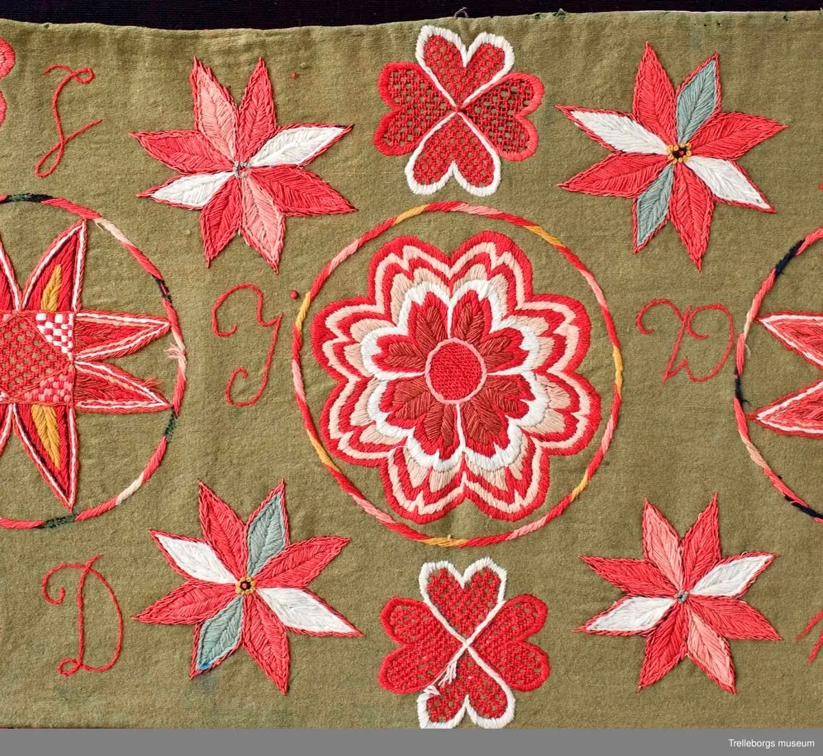 Bottentyg är grön vadmal. Tre stora ringar i kontur utgör huvudmotiv. I ringen i mitten är en stor blomma med 8 kronblad utfyllnad. I de båda ringarna vid sidan är broderat en spetsuddig stjärna med 8 vingpar. Dess centrum är en snedställd kvadrat, sydd i gallerliknande konstsöm. Utmed agedynans långsidor är broderat olika blomsterstjärnor, pionliknande blommor och en blomliknande rundning av 4 st hjärtfigurer. Färger: vitt, gult, svart, blågrått samt många olika nyanser i rött. Baksidan tegelröd yllevävnad. 
Enligt katalogen märkt I.W.D.S.  SL. Hjärtrosetter och hjärtan. 
Enligt Ernst Fischer, Årsbok från Malmö museum 1971, sid 180: En åkdyna i Tbgs museum har som mittmotiv en runduddig stjärna, omgiven av en ring samt en hjärtrosett över och under, flankerad av spetsuddiga stjärnor. T.h. och v om mittmotivet stora spetsuddiga stjärnor inom ringar. I hörnen varierande blomformer. De ganska svårtydda initialerna skulle kunna tydas som LWD IVH, ehuru bokstäverna då icke är placerade i rätt ordning. IVH skall i så fall beteckna I Vämmenhög.