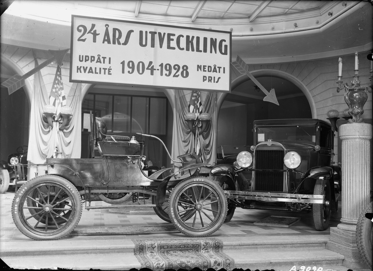 Bilar på utställning i Ostermans marmorhallar. Skylt: "24 års utveckling. Uppåt i kvalité 1904-1928 nedåt i pris". Till höger i bild står en Oldsmobile 1928.