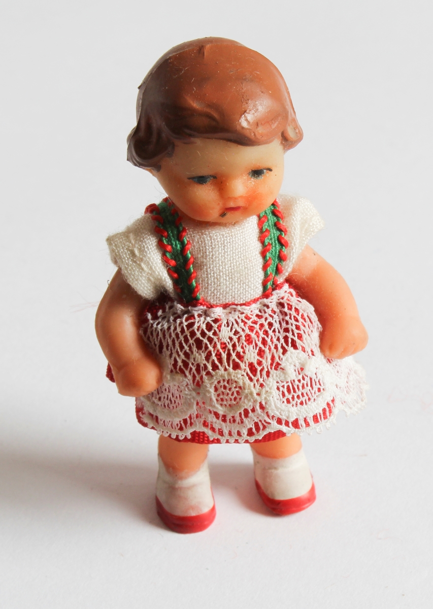 Gitt av Gerd Berit Lie
Hjemmelaget dukkehus av pappeske med to rom. Tapesert, Laget av far, Lorentz Lie (f.1908). Ulike møbler og dukker hører til med til huset. Totalt 35 deler. Det er egen spisestue i tre, bestående av 9 deler (spisebord, stoler, veggur, bokhylle, skap). Det er bad bestående av 3 deler (badekar, servant og toalett i turkis plast). Tilsammen 8 dukker i miniatyr størrelse. Egen kjøkken del med 6 ulike deler (kjeler, kjøkkenbord, fjøler, vase). Og 8 små plastskjeer med skuff.