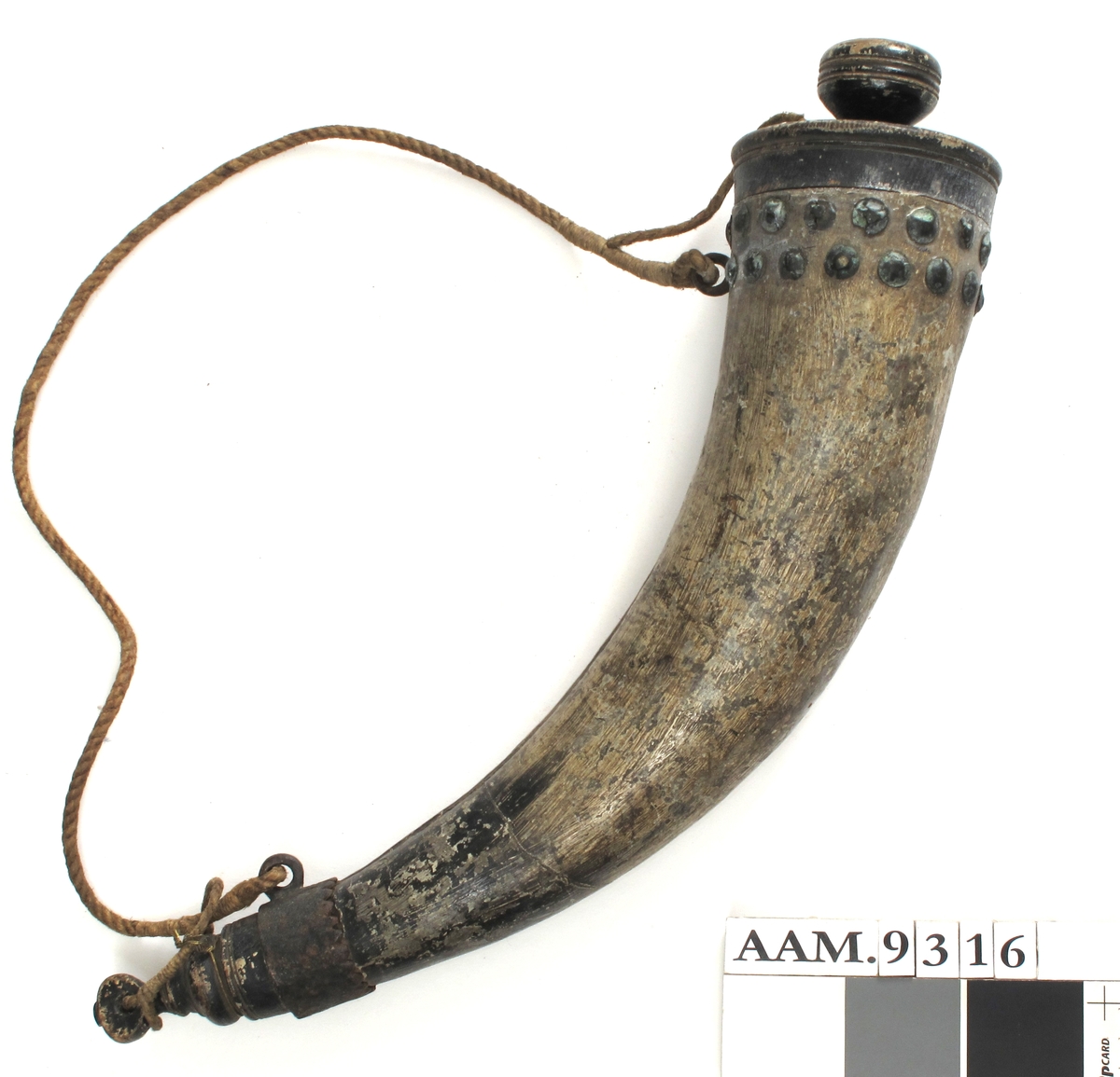 Krutthorn, imitert horn av malt tre,  med sortmalt trelokk og bunn, jernbeslag og   messingknapper. Horn malt i hornimitasjon med lysbrune striper, sort i nedre del.  Skjøt langs innsiden av buen. Sort  dreiet  lokk med nedsenket toppflate, stor dreiet knott med skrugjenger.  Under trelokket to rader med messingknapper. I nedre del et jernbeslag med takker langs overkanten, i dette en jernring  for feste av bæresnoren av tau.