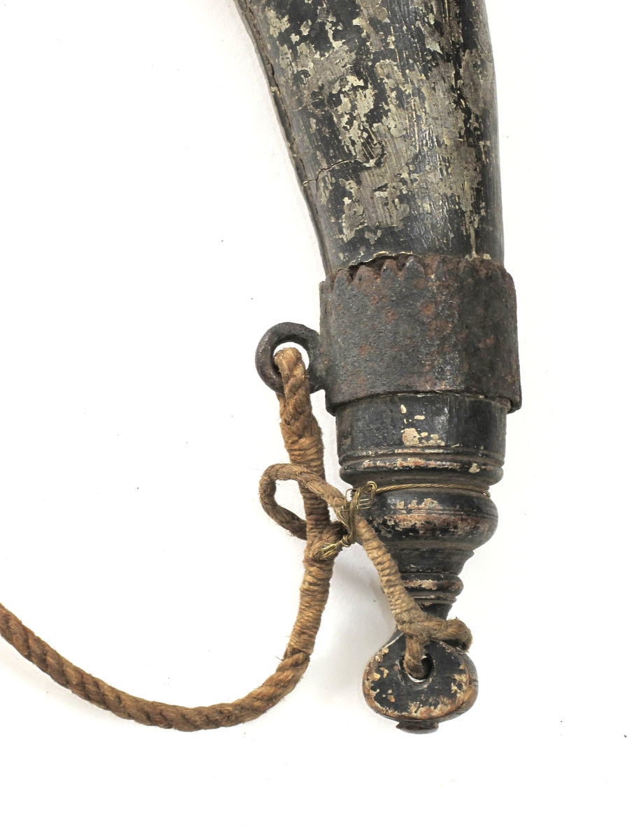 Krutthorn, imitert horn av malt tre,  med sortmalt trelokk og bunn, jernbeslag og   messingknapper. Horn malt i hornimitasjon med lysbrune striper, sort i nedre del.  Skjøt langs innsiden av buen. Sort  dreiet  lokk med nedsenket toppflate, stor dreiet knott med skrugjenger.  Under trelokket to rader med messingknapper. I nedre del et jernbeslag med takker langs overkanten, i dette en jernring  for feste av bæresnoren av tau.