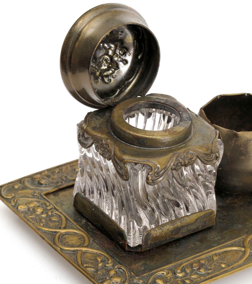 Skrivestell. Presset  messing, 2 blekkhus av  pressglass. Rektangulær messingplate med presset ornamentbord langs kanten og 4 små dreide føtter. Presset dekorativt mønster.