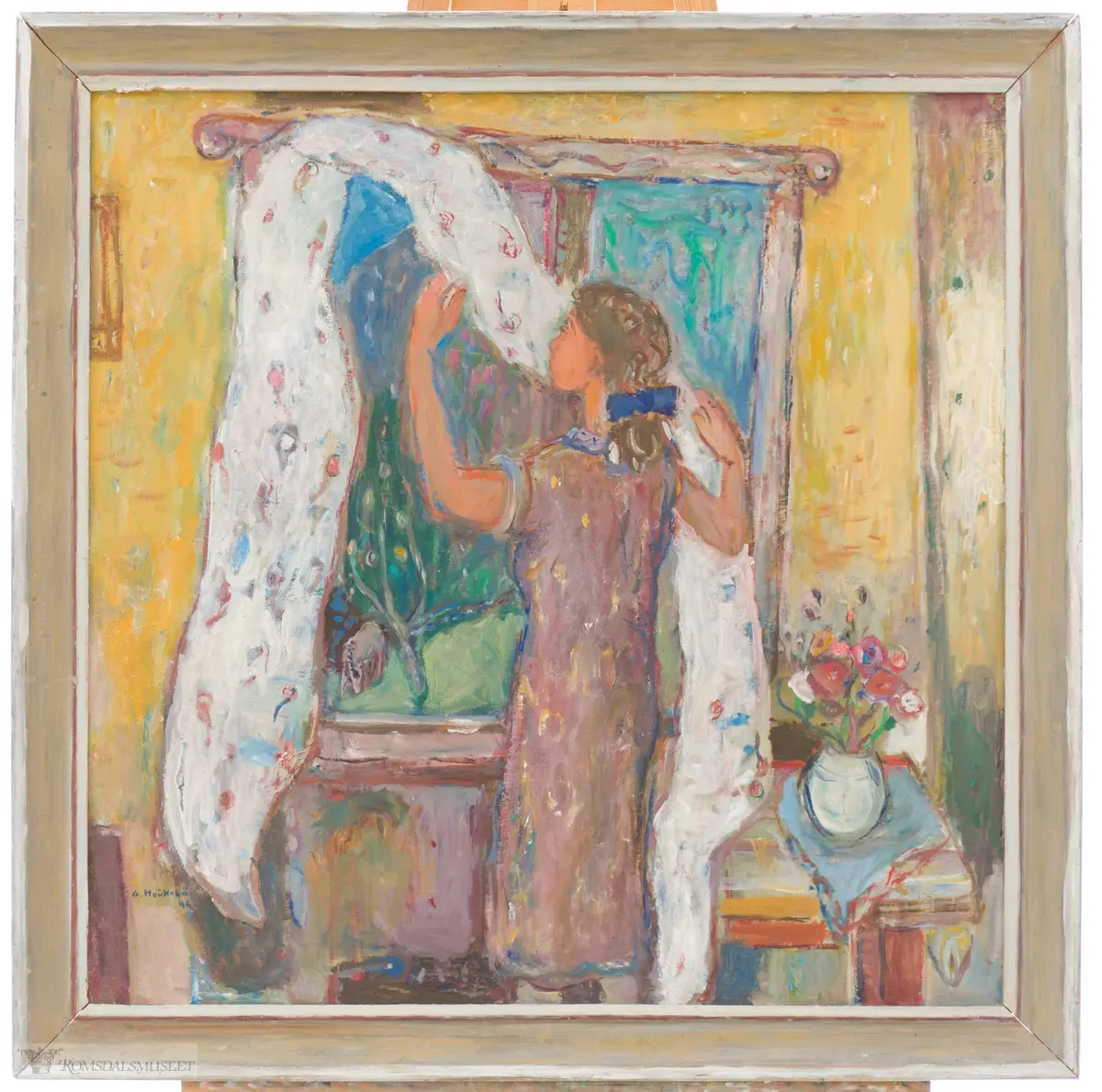 En kvinne henger opp en lys gardin i et vindu. utenfor kan en frodig hage sees. Ved kvinnens høyre side, et lite bord med en hvit vase med sommerblomster i.