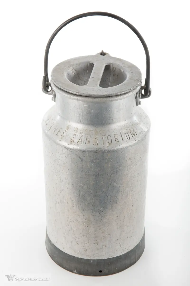 Melkespann i aluminium med lokk og hank. Lokket er festet i spannet med kjetting. Spannet har forsterket bunn.
