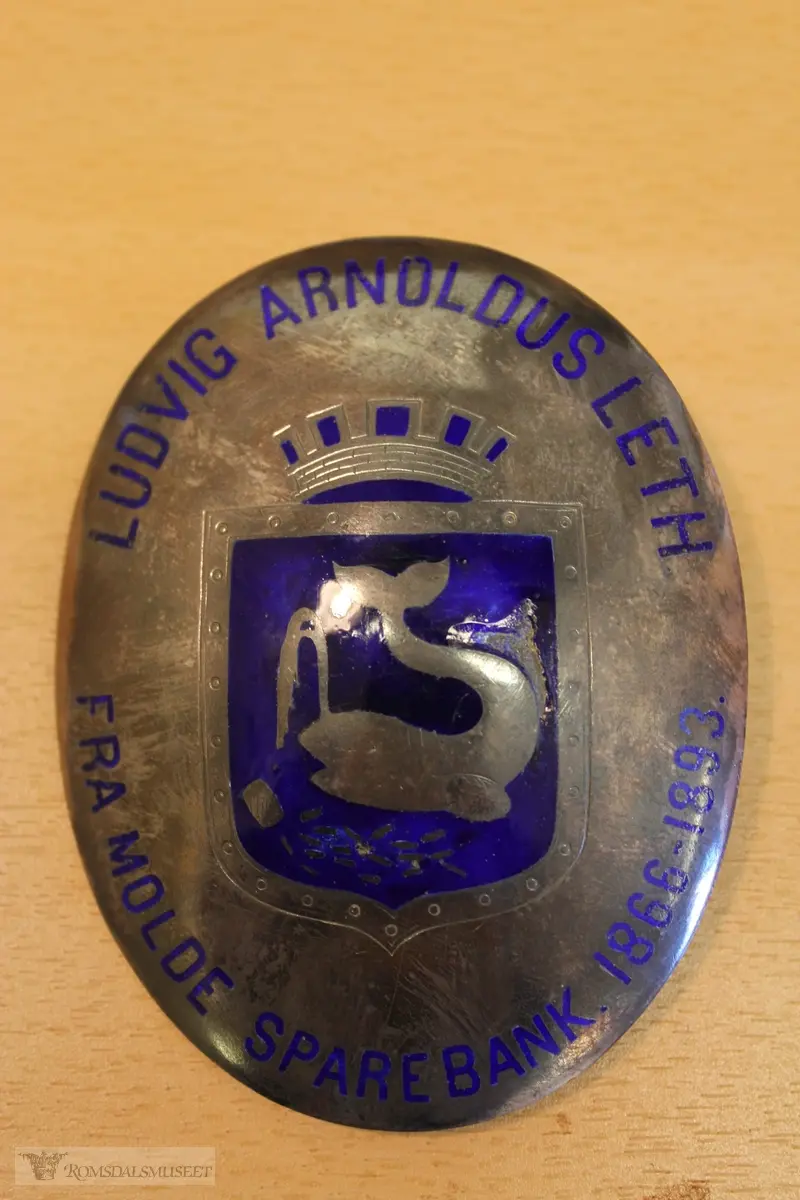 To emaljerte medaljonger: Byvåpen og Romsdalshorn.