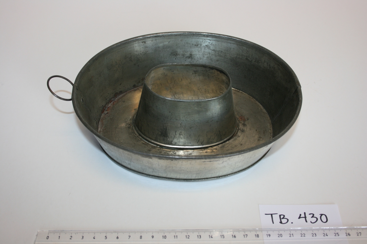 Den ovale puddingformen er svakt konisk og har flat bunn med et ovelt hull med mål B: 5 cm og L: 8 cm. 
Produktet er et bikksmedarbeid.
