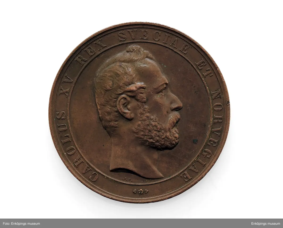 Medalj av kopparlegering, åtsida: Karl XV i högerprofil med text runtom, " CAROLUS XV REX SVECIAEN ET NORVEGIAE". Frånsida: allegorisk kvinnogestalt med lagerkrans och uggla (= Pallas Athena/ Minerva) invid en sockel med tre kronor i en cirkel och en oljelampa (?) på en liten kolonn; inskription:  ACADEMIA CAROLINA SACRA SAECULARIA ITERUM CONCILIATRIX CELEBR. MD CCCLXV III samt gravörens namn, J. Ericsson.