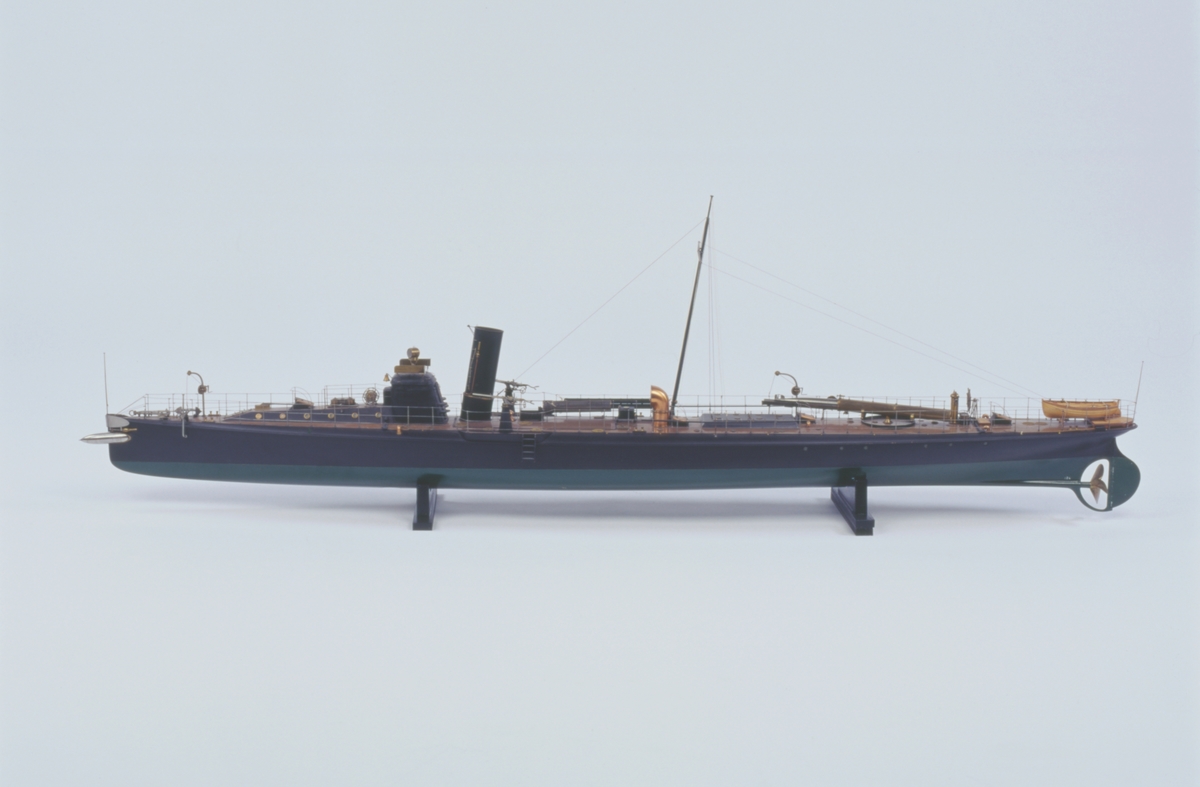 Fartygsmodell lamellbyggd. 

Fullständig däcksinredning, roder, metallpropeller, däckstub av metall med torped av järn, stävtub med torped av järn. 1 skorsten, oval. Riggad mast med vimpel, flaggspel med flagga, gösstake med gös. Fallrepstrappor. Ventilatorer och luckor av koppar. Svartmålad, grön botten, korkfärgat däck. 2 kulsprutor av järn i tamburer. 
Jolle, bordlagd på spant, klink, fullständigt inredd, roder med rorkult och skädda, 4 st åror, 1 båtshake, fernissad. Stativ 2 metallpelare.