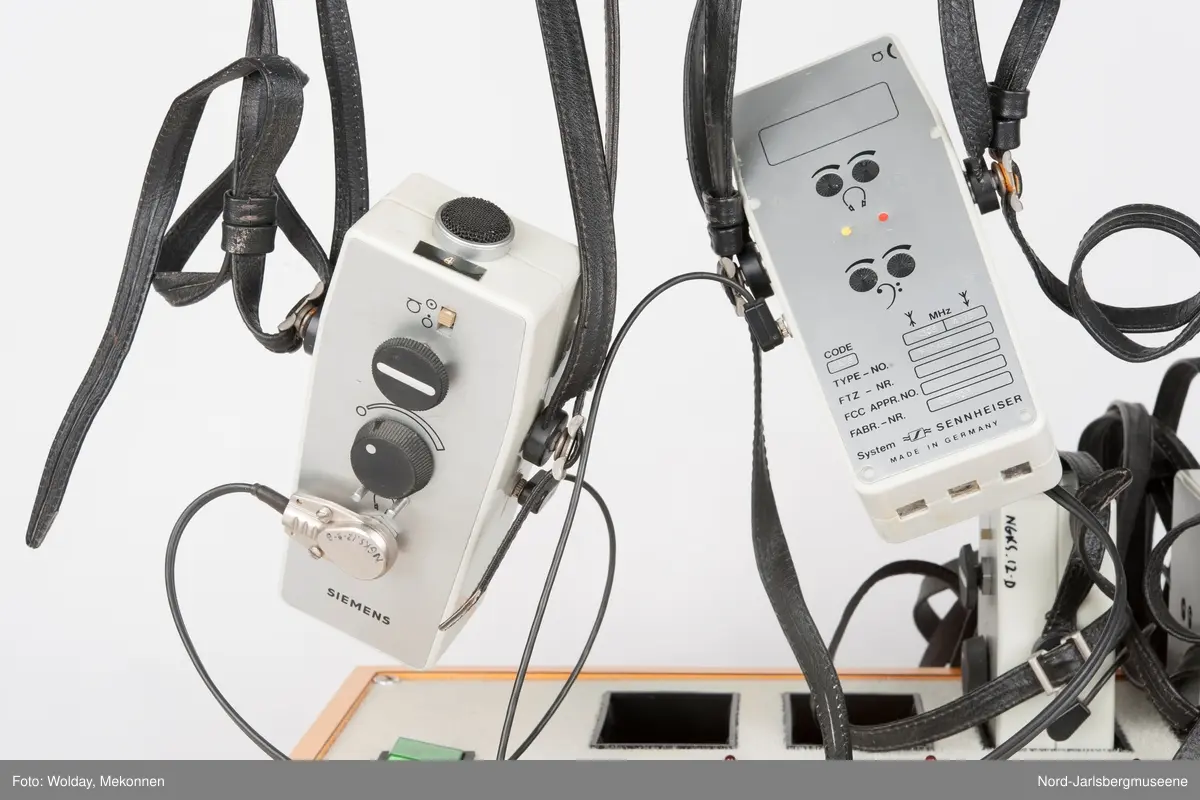 Rektangulær kasse med strømbryter og ladehull for 10 teleslynger. Kassern er oransje, telsyngene i plast og metall. Her følger det 6 teleslyngapparater med.
10 deler tilsammen